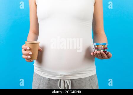 Nahaufnahme einer schwangeren Frau mit einem Papierbecher und einem Haufen Blasen mit Pillen auf buntem Hintergrund mit Kopieplatz. Behandlungskonzept. Stockfoto