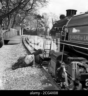 Schauspielerin Diana Rigg vor Ort für eine neue Serie der TV-Actionserie 'The Avengers'. In dieser Aufnahme wird sie für die Episode "die Totengräber" an die Schienen einer Miniatureisenbahn auf Lord Grettons Stapleford Park Estate in der Nähe von Melton Mowbray, Leicestershire, gebunden. Stockfoto