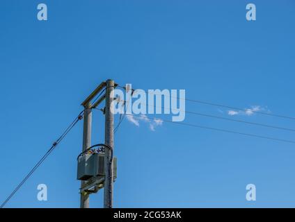 Ein Stromwandler auf zwei hölzernen Telegrafenmasten mit blauem Himmel Hintergrund. Stockfoto