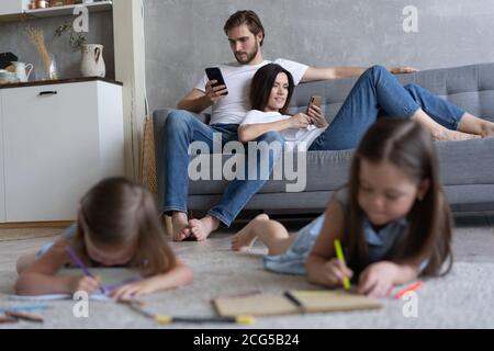 Kinder Schwestern spielen Zeichnung zusammen auf dem Boden, während junge Eltern zu Hause auf dem Sofa entspannen, kleine Mädchen Spaß haben Stockfoto