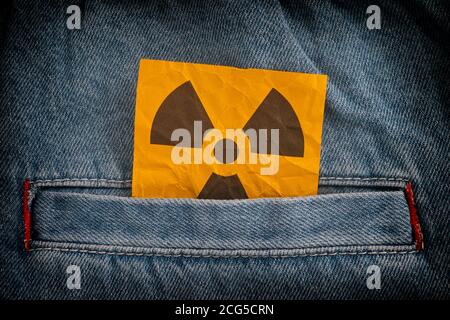 Strahlungswarnschild ragt aus einer Jeans-Tasche heraus. Nahaufnahme. Stockfoto