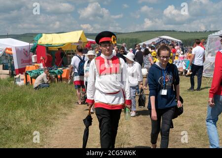 Ein Mann in russischer Volkstracht, der während des Volksfestes Karatag am Ufer eines großen Sees die Marktstraße entlang läuft. Stockfoto