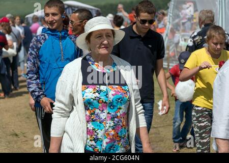 Eine ältere Frau geht vor jungen Menschen während des Volksfestes Karatag am Ufer eines großen Sees. Stockfoto