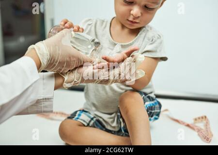 Arzt legt Handdesinfektionsmittel auf Babyhände. Einem kleinen Jungen Händewaschen und Hygiene beibringen. Körperliche Untersuchung des 1-jährigen Jungen. Gut, Baby Stockfoto