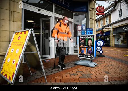Caerphilly, Wales, Großbritannien. Ein Mann verlässt ein Geschäft mit einer Maske geht vorbei an einem ' Gesichtsmaske auf Verkauf hier ' Zeichen in der Stadt Caerphilly in Südwales, die Stockfoto