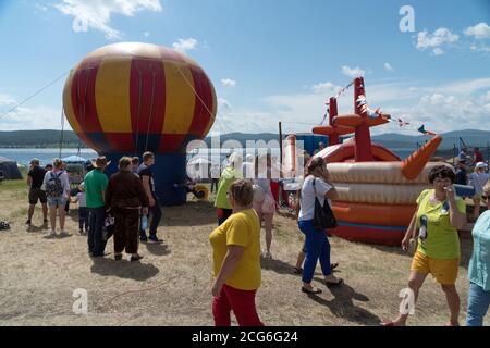 Während des Musikfestivals Karatag am Ufer eines Sees laufen die Menschen an einem Kinderspielplatz mit aufblasbaren Attraktionen vorbei. Stockfoto