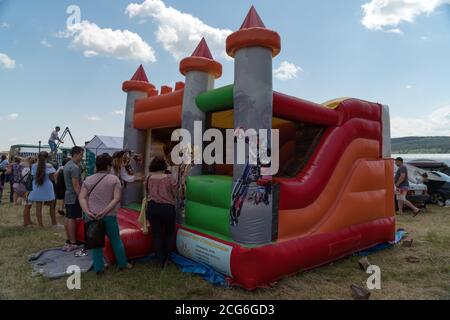 Beim Festival Karatag am Ufer des Sees stehen Menschen in der Nähe eines aufblasbaren Kindertrampolins in Form einer Burg. Stockfoto