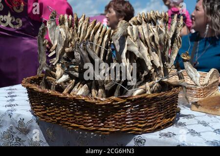 Gesalzene, getrocknete Fischschaber, aufgereiht auf einem Draht, liegt in einem Weidenkorb, der auf dem Tisch gegen Frauen steht. Stockfoto