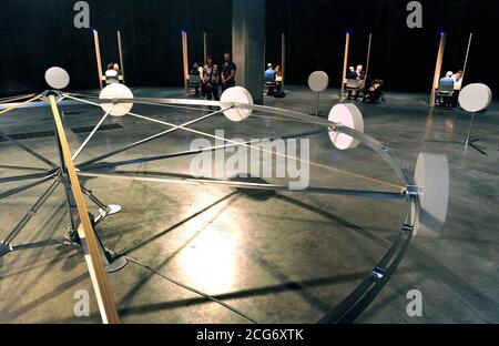 Eine allgemeine Ansicht der Jon Fawcett-Installation "EIR", sechs Kabinen, die von Psychikern bemannt sind, die Mitglieder der Öffentlichkeit für eine mögliche Rekrutierung bei einer geheimen Organisation abschirmten, und Whum, ein 7 Meter breites, langsam drehendes Rad mit neun zylindrischen Gefäßen, die nicht offengelegte Materialien auf seinem Rand enthalten, umgeben von zehn weiteren, Das ist Teil der Undercurrent: Young People's Ausstellung in der Tate Modern, London. Stockfoto