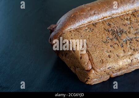 Roggenbrot mit Kümmel auf schwarzem Hintergrund. Seitenansicht von frisch gebackenem hausgemachtem Brot, bestreut mit Kreuzkümmel. Speicherplatz kopieren. Selektiv Stockfoto