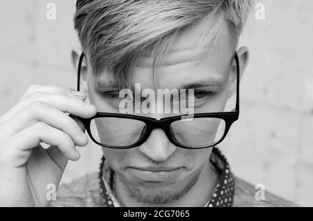 Blonde Mann mit kleinem Bart zieht seine Brille in Überraschung.Junge Mann mit lustigen Haarschnitt in der Brille Grimasse machen - lustige Gesicht. Emotionen und si Stockfoto