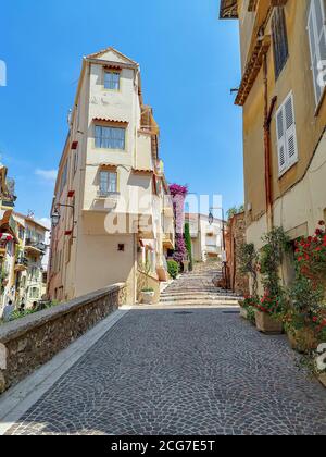 Leere schmale Straße auf einem Hügel mit Steinpflaster und altem Gebäude in gelben Farben mit Balkonen, die mit grünen Pflanzen in Blumentöpfen in Nizza dekoriert sind. Stockfoto