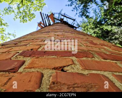 Blick von unten auf den alten, Vintage-Stil roten Ziegelwasserturm gegen blauen Himmel und Baumkronen an einem sonnigen Tag. Stockfoto