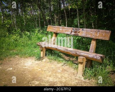 Vorderansicht einer leeren Holzbank in einem einsamen grünen Park auf einem Hügelpark in der Nähe der Karpaten. Sonniger Tag, blauer Himmel. Stockfoto