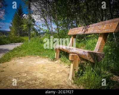 Seitenansicht einer leeren Holzbank in einem einsamen grünen Park auf einem Hügelpark in der Nähe der Karpaten. Sonniger Tag, blauer Himmel. Stockfoto