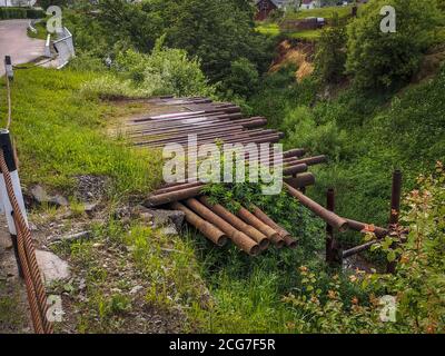 Halbkonstruierte Brücke aus rostigen Rohren, die aus dem hohen Hang eines Bergbaches in einem ländlichen Gebiet der Ukraine herausragen. Stockfoto