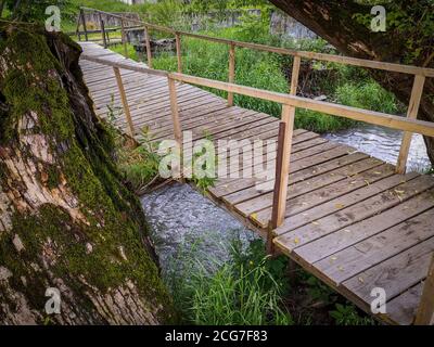 Neue einfache Holzbrücke aus Brettern mit Geländern über dem Bergfluss in einer ländlichen Gegend. Stockfoto