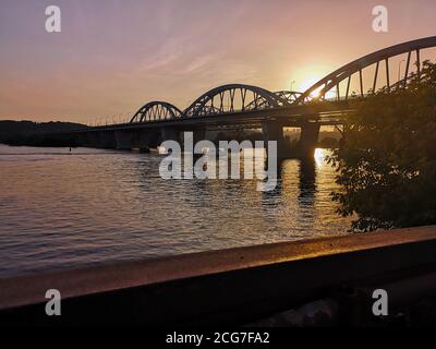 Blick vom linken Ufer des Dnjepr über die Darnytskyj-Brücke und das rechte Ufer der Stadt Kiew. Wunderschöner, farbenfroher Sonnenuntergang. Stockfoto