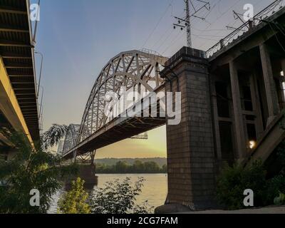 Blick vom linken Ufer des Dnjepr über zwei Brücken. Darnyzkyj Brücke und rechten Ufer der Stadt Kiew bei Sonnenuntergang. Stockfoto