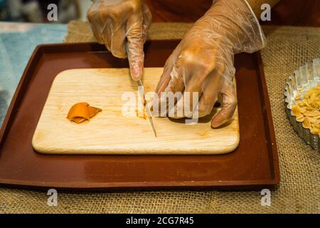 Eine Nahaufnahme der Hand einer Frau mit einem Messer geschnitten getrocknete Mandarine Schale auf einem hölzernen Schneidebrett. Food-Konzept Stockfoto