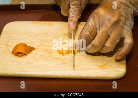 Eine Nahaufnahme der Hand einer Frau mit einem Messer geschnitten getrocknete Mandarine Schale auf einem hölzernen Schneidebrett. Food-Konzept Stockfoto