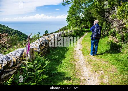 Ein männlicher Wanderer mittleren Alters macht Fotos entlang des South West Coast Path in der Nähe von Lynton in North Devon. Stockfoto