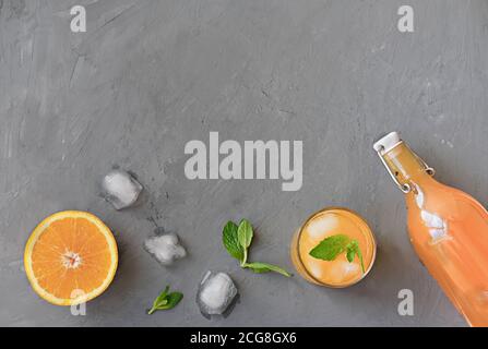 Orangen- und Orangensaft in einer Flasche und in einem hohen Glas. Minzblätter auf grauem Hintergrund. Eiswürfel schmelzen. Sommerfrische saftige Früchte. Kalter Sommer drin Stockfoto