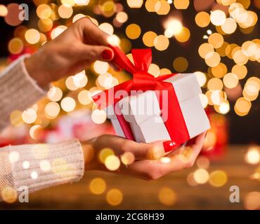 Detail der Frau Hand Auspacken Weihnachtsgeschenk mit verschwommenen Lichtflecken um. Feier von Heiligabend, gemütliche Atmosphäre Stockfoto
