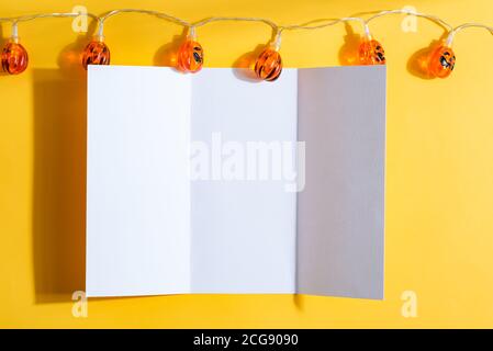 Blank imitierten weißen Papier dreifach Broschüre A4 Broschüre verziert Hallowen Girlande aus kleinen Kürbissen auf einem gelben Hintergrund, Kopierraum. Draufsicht. Er Stockfoto