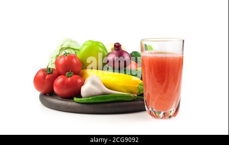 Ein Glas frischen Gemüsesaft und eine große Auswahl an frischem Gemüse auf einem runden Tablett auf weißem Hintergrund. Stockfoto