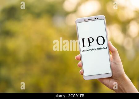 Anfängliches Public Offering-Konzept. Junge weibliche Hand hält Handy & zeigt IPO, die auf dem Bildschirm im Freien Hintergrund mit Cop angezeigt wird Stockfoto