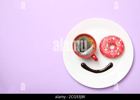 Lächeln Gesicht aus Teller mit Donut, Schokoladensauce und Kaffee auf violettem Hintergrund Stockfoto