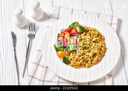 Veganer mac und Käse mit Hefesoße und Gemüsesalat auf weißem Teller auf weißem Holztisch mit Silberbesteck, Landschaftsblick Stockfoto