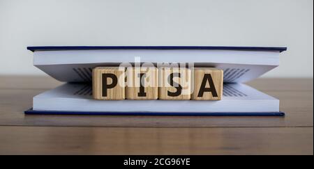 Würfel in einem Buch bilden das Wort 'PISA' als Symbol für die internationale Pisa-Studie. Buch liegt auf einem Holztisch in einer Bibliothek. Schöne weiße Rückenfarbe Stockfoto