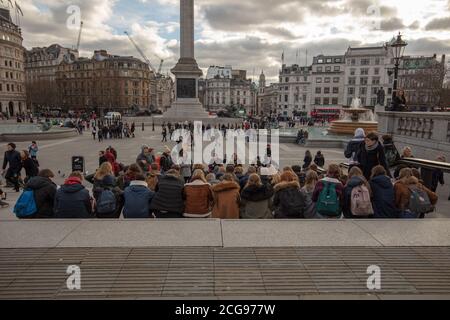 Eine Gruppe junger Studenten sitzt zusammen auf den Stufen des Trafalgar Square London, mit Nelson's Column im Hintergrund. Stockfoto