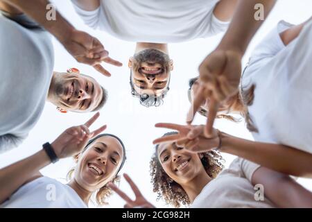 Gruppe junger schöner Freunde, die auf die Kamera herunterschauen Zeigefinger V-Zeichen - Low-Winkel-Ansicht von fünf niedlich Die Menschen, die den Sieg tun, unterschreiben zusammen Stockfoto