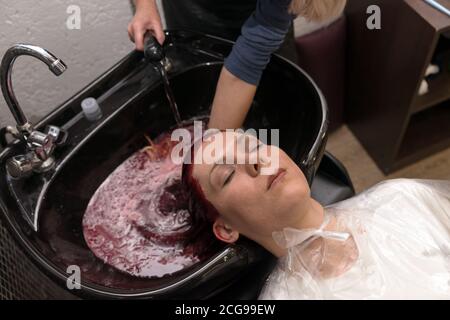 Weibliche Friseur wäscht den Kopf der Klientin auf einem speziellen Waschbecken nach dem Färben der Haare im Friseursalon im realen Arbeitstag. Stockfoto