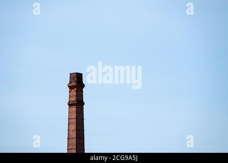 Roter Ziegelstapel des alten Schornsteins auf der großen verlassenen Mühle, klarer blauer Himmel am Morgen. Stockfoto