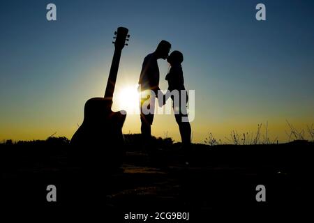 Glückliche und starke junge Familie auf Hochzeitsreise. Silhouetten von küssen Brautpaar auf dem Hintergrund des Sonnenuntergangs Himmel und das Meer in der Sonne, während w Stockfoto