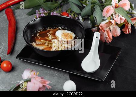 Asiatische Nudelsuppe, Ramen mit Huhn, Tofu, Gemüse und Ei in schwarzer Schüssel. Schieferhintergrund Stockfoto