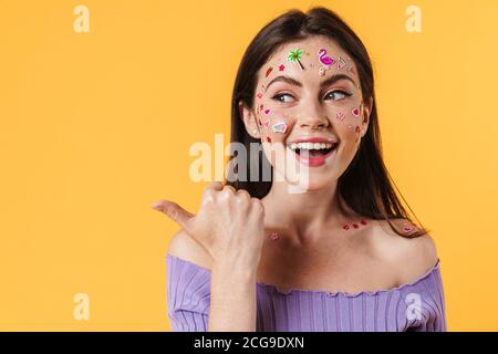 Bild von freudiger Frau mit Aufklebern auf Gesicht lächelnd und Zeigen Sie den Finger isoliert über die gelbe Wand zur Seite Stockfoto