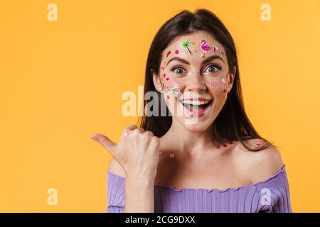 Bild von freudiger Frau mit Aufklebern auf Gesicht lächelnd und Zeigen Sie den Finger isoliert über die gelbe Wand zur Seite Stockfoto