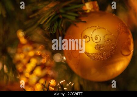 Ein goldenes Ornament mit Funkeln hängt von Christbaumglied Mit einem Pinienkegel im Hintergrund Stockfoto