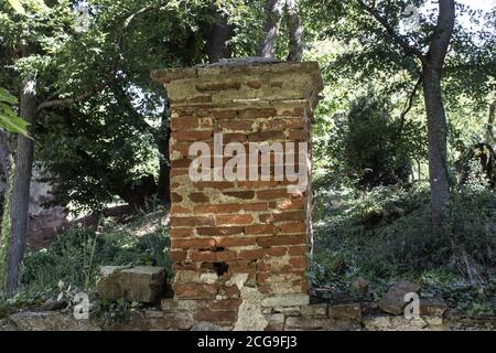 Ein Ziegelzaunpfosten. Bäume hinter der Ziegelmauer. Stockfoto