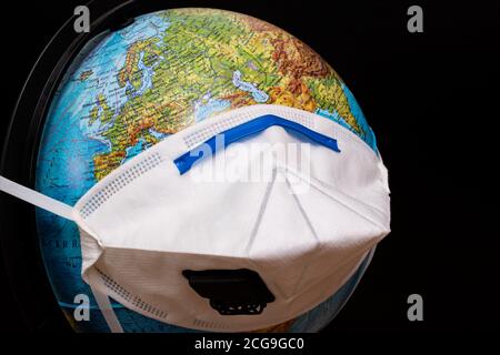 Globus in medizinischer Schutzmaske auf schwarzem Hintergrund Stockfoto