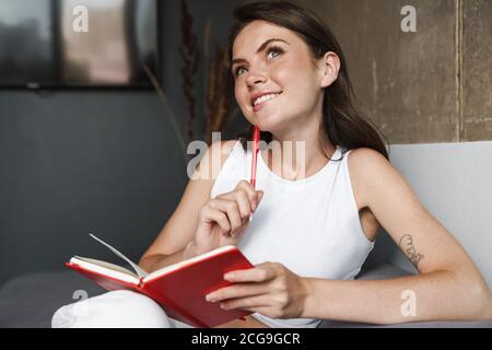 Schöne junge Frau sitzend auf einer Couch denken und schreiben Notizen in einem Tagebuch Stockfoto