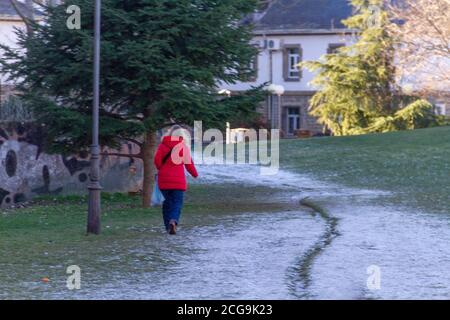 Frau in einem roten Mantel geht auf dem Schnee Das hat begonnen, auf den Parkweg zu fallen Stockfoto