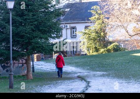 Frau in einem roten Mantel geht auf dem Schnee Das hat begonnen, auf den Parkweg zu fallen Stockfoto
