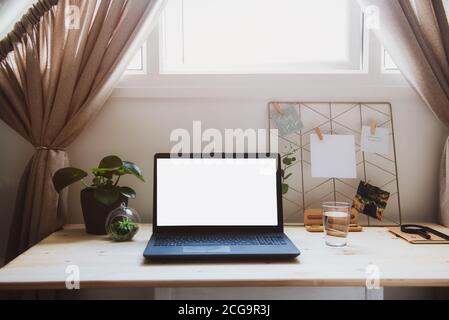 Moderner minimalistischer Arbeitsplatz mit Laptop-Modell mit weißem leerem Bildschirm auf Holzschreibtisch mit Moodboard mit pinierten Notizen und Foto, grüne Pflanzen bei der Arbeit Stockfoto