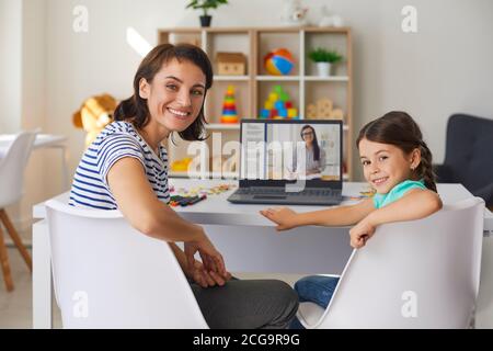 Lächelnd Mutter und Tochter Blick auf Kamera, während mit online Unterricht mit Privatlehrer Stockfoto